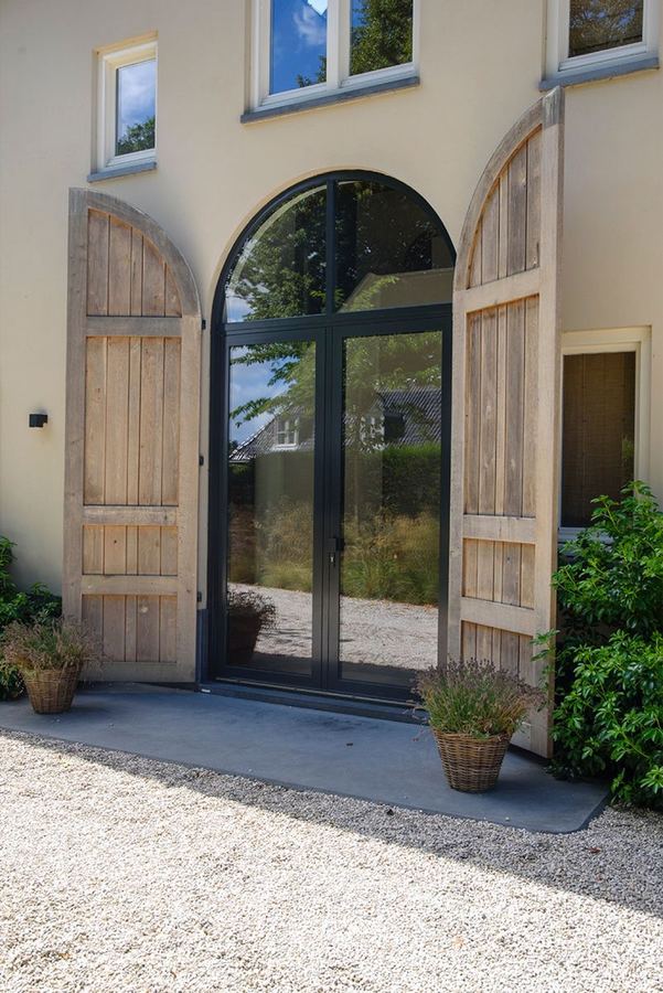 Slanke aluminium voordeur in een rond gemetselde entree met houten poorten